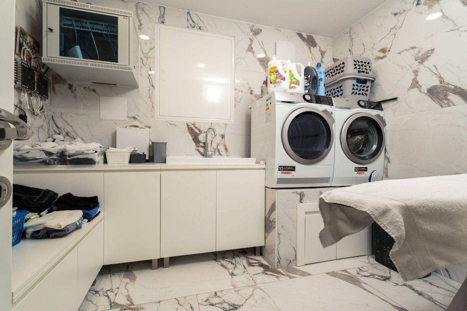 Praktischer Hauswirtschaftsraum mit Waschmaschinen, Spülbecken und eleganten Marmorfliesen.
