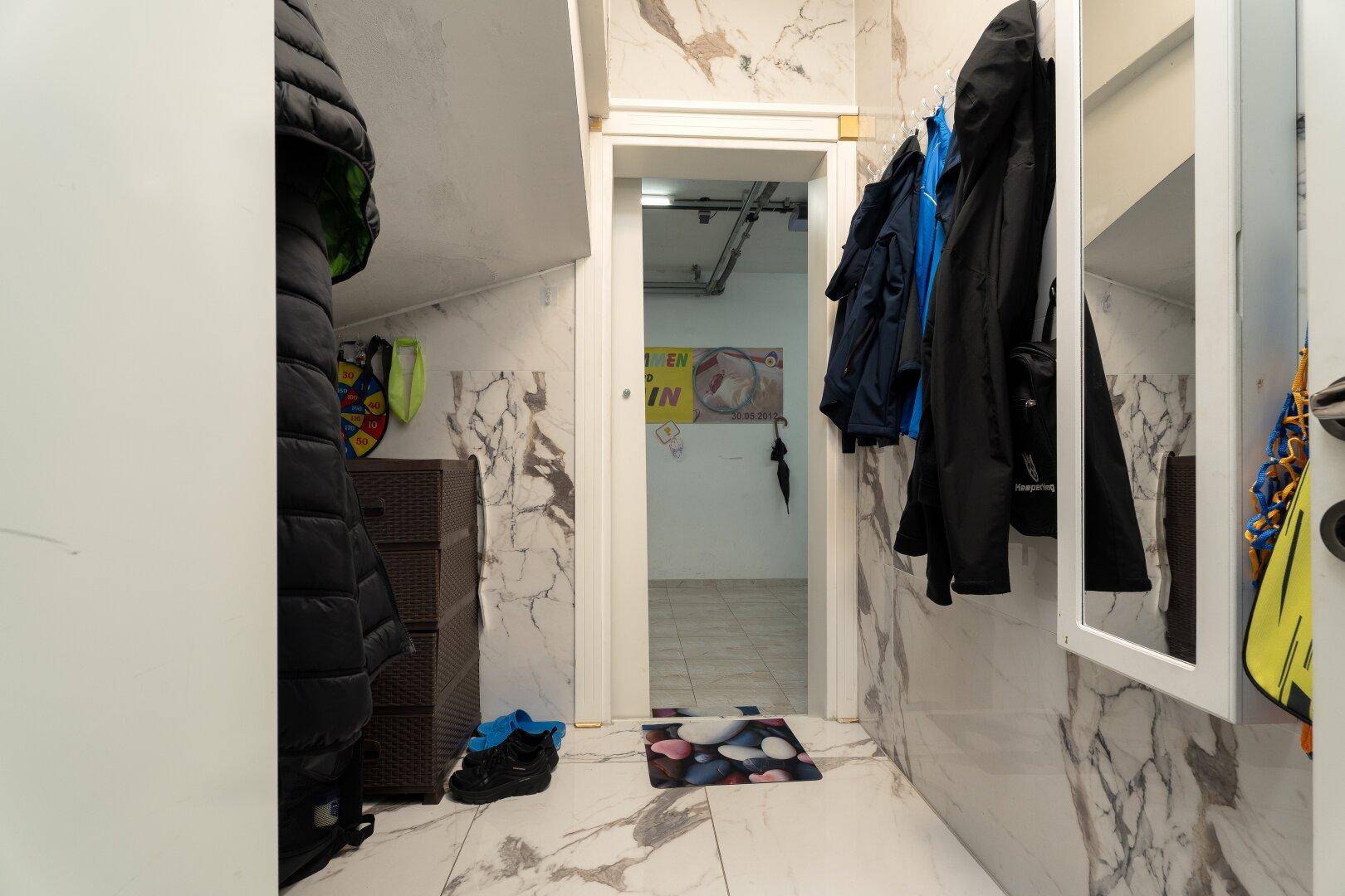 Kleiner Eingangsbereich mit Marmorfliesen, Garderobe und einem Spiegel, der zu weiteren Räumen führt.