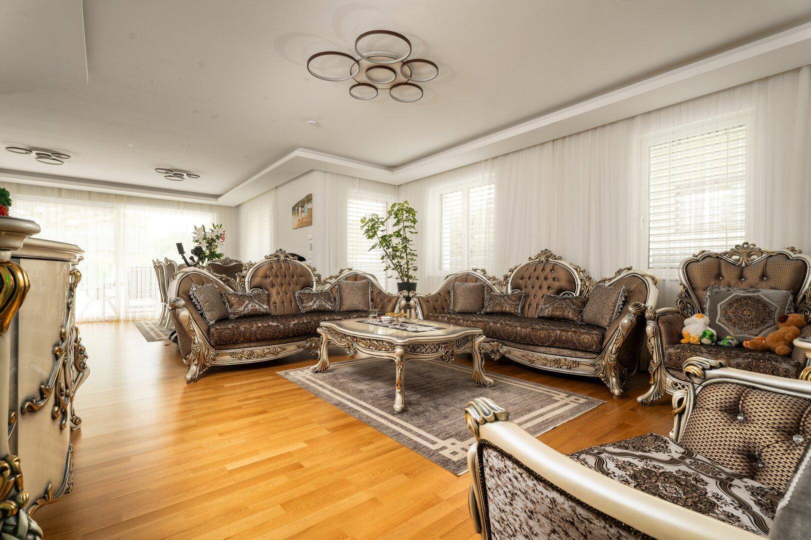 Klassisch eingerichtetes Wohnzimmer mit opulenten Sofas, Holzboden und großen Fenstern für viel Helligkeit.