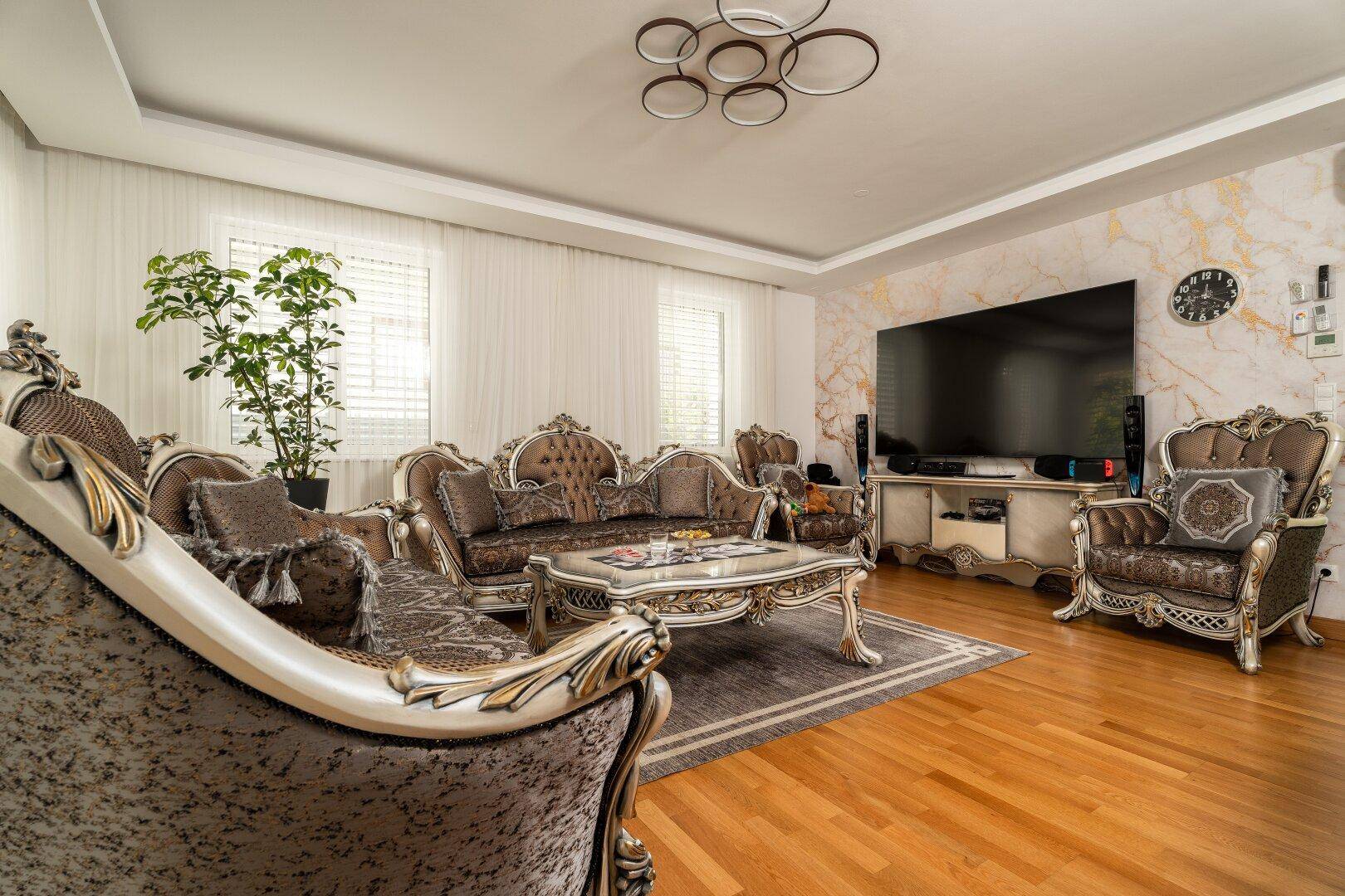 Elegantes Wohnzimmer mit großem Wandfernseher, luxuriösen Möbeln und einem hellen Holzboden.