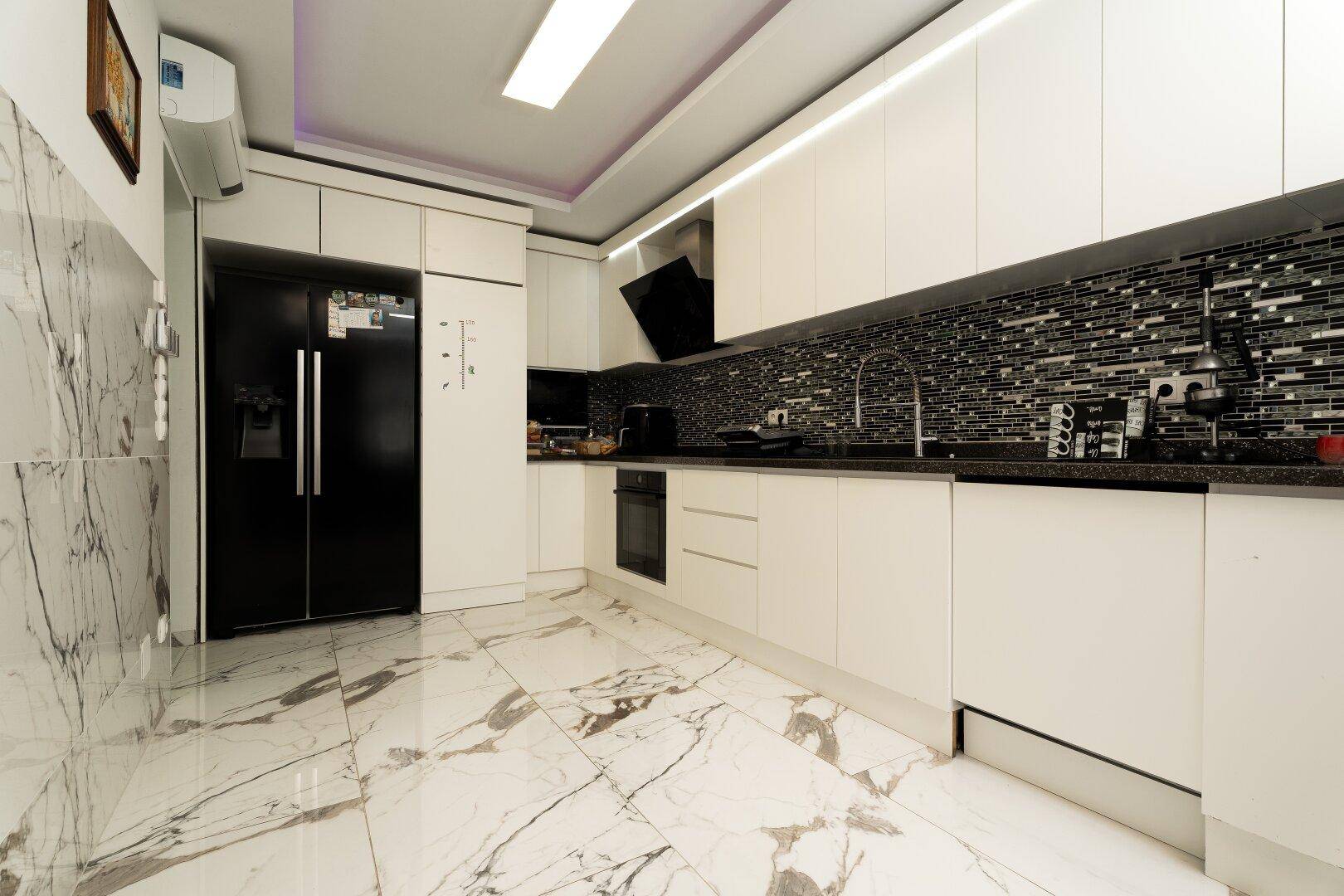 Helle und moderne Küche mit weißen Schränken, großem schwarzem Kühlschrank und Marmorboden.