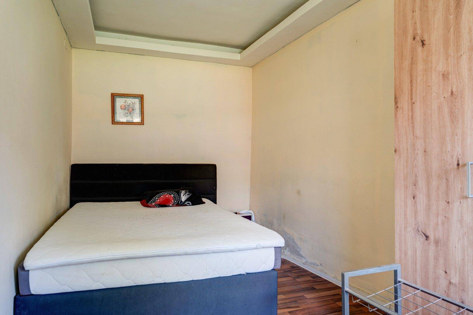 Schlafzimmer mit Doppelbett, Holzwand und einfacher Einrichtung.