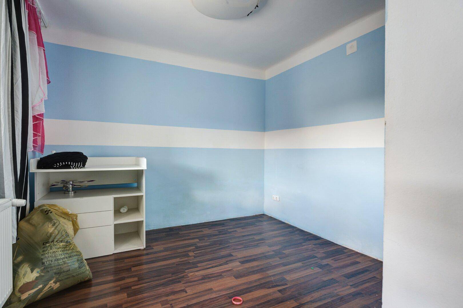 Kinderzimmer mit blau-weiß gestreiften Wänden und Laminatboden.