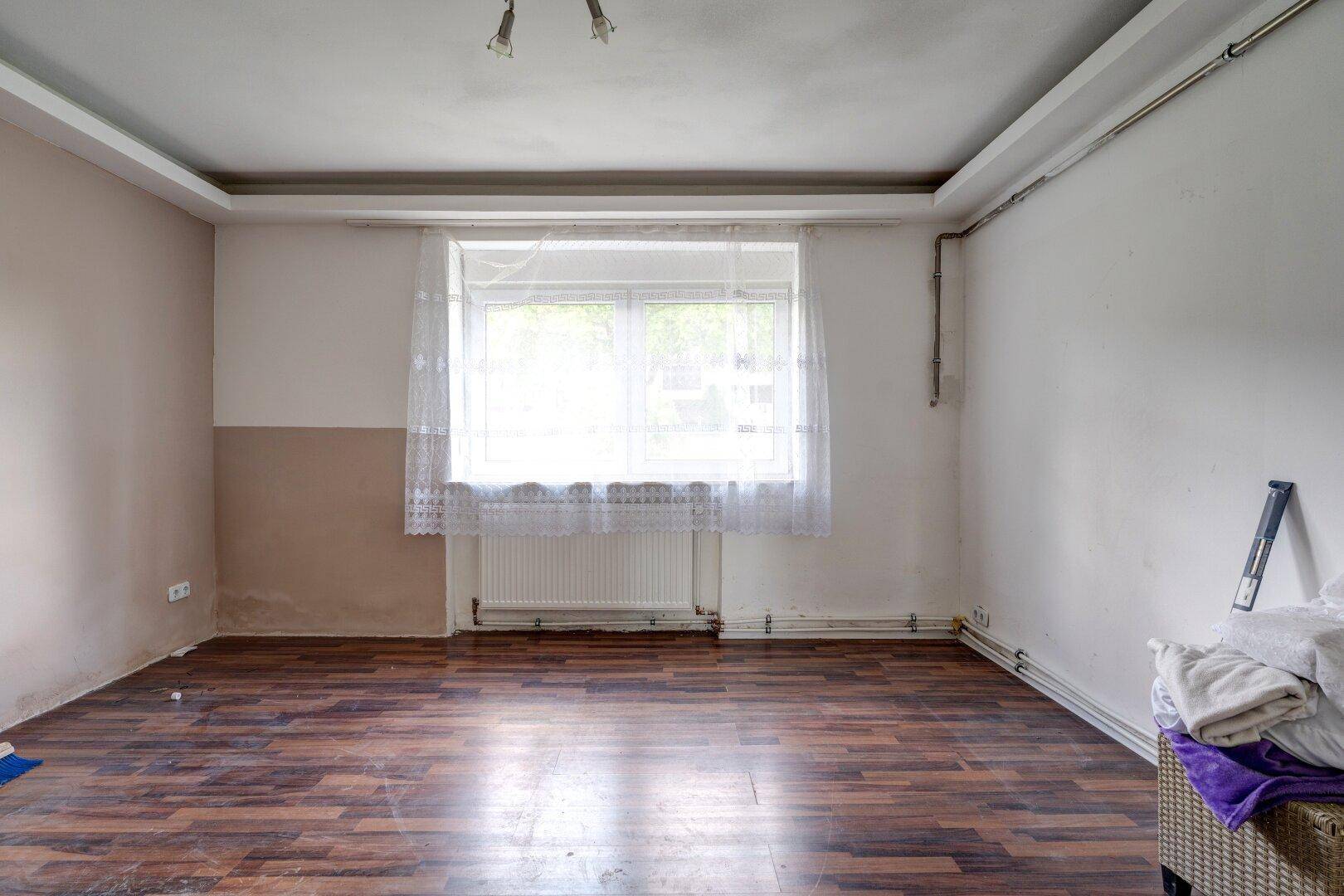 Leeres Zimmer mit Laminatboden, Fenster und schlichten Wänden.