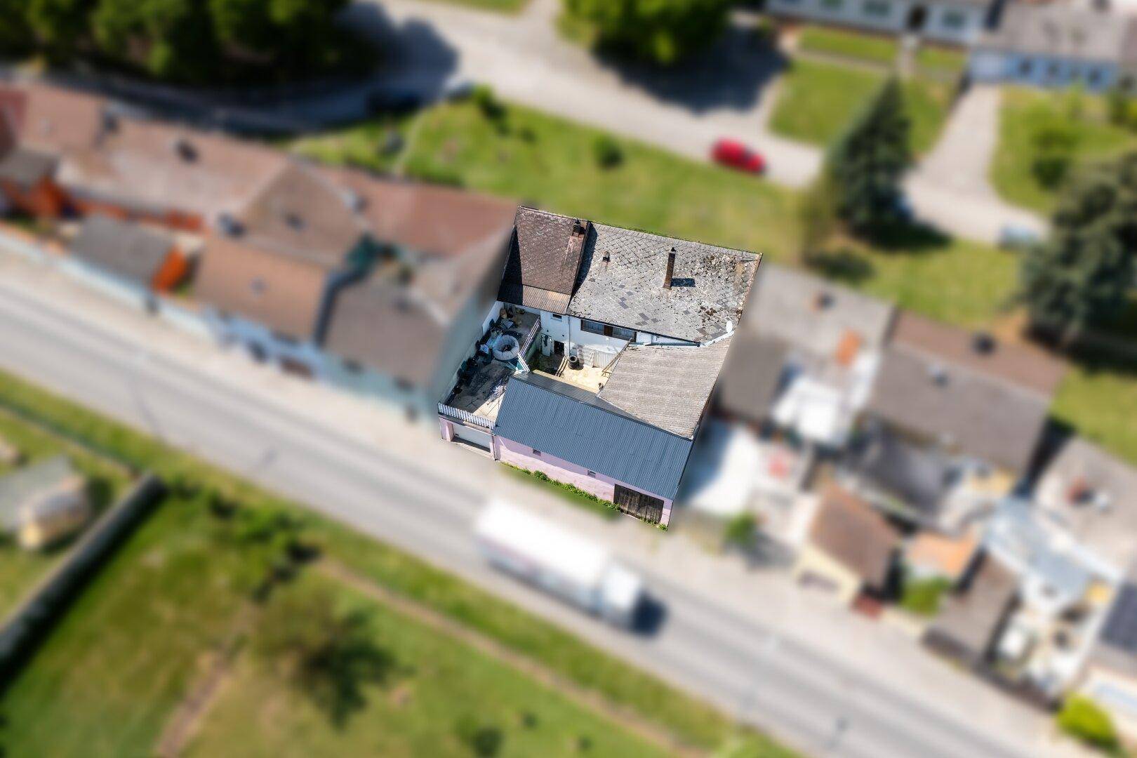 Luftaufnahme des Wohnhauses in einer ländlichen Umgebung mit einer Straße und Fahrzeugen im Vordergrund.