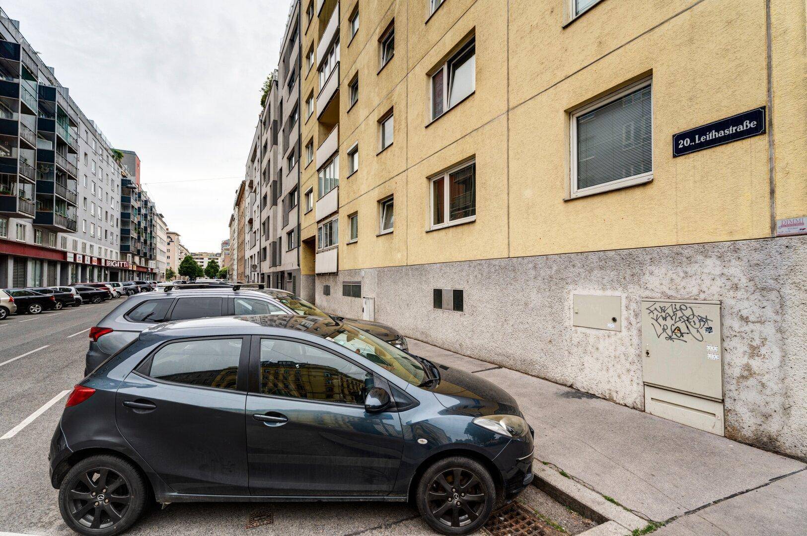 Straßenansicht eines Wohngebäudes mit parkenden Autos und Straßenschild.