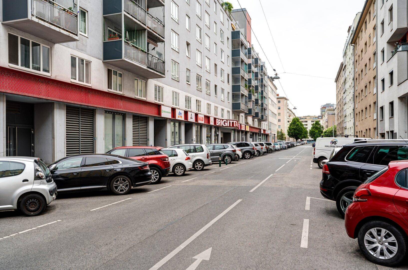 Stadtansicht mit mehrstöckigen Wohngebäuden und parkenden Autos entlang der Straße.