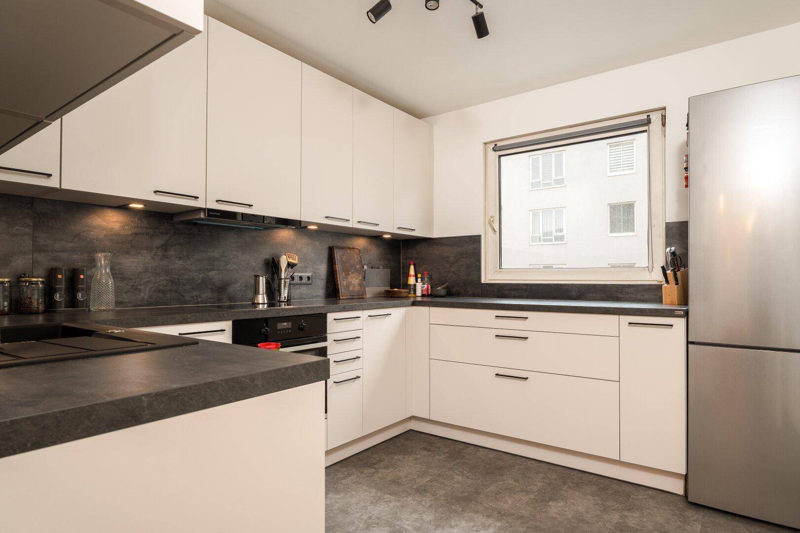 Moderne Küche mit weißen Schränken, dunkler Arbeitsplatte und Fensterblick.