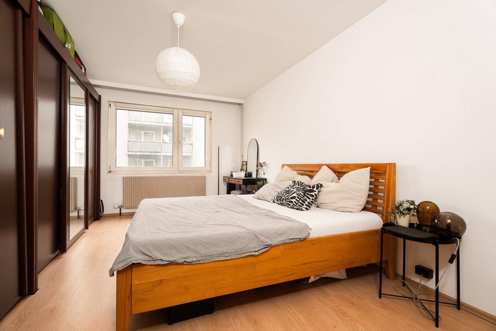 Schlafzimmer mit Holzbett, großem Kleiderschrank und Fenster mit Blick nach draußen.