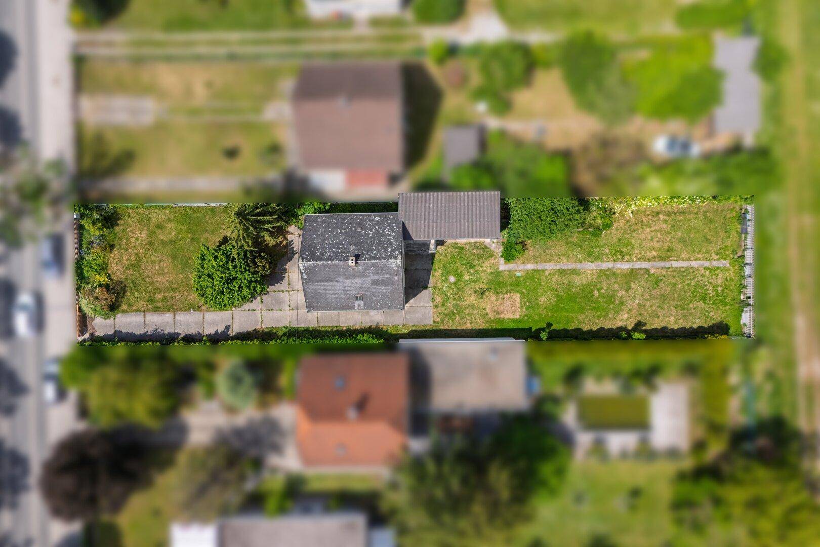 Vogelperspektive eines Hauses mit langem Grundstück, umgeben von Gärten und Nachbarhäusern.