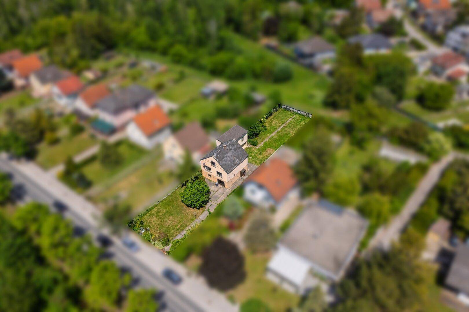 Luftaufnahme eines Einfamilienhauses mit großem Garten in einer grünen Wohngegend.