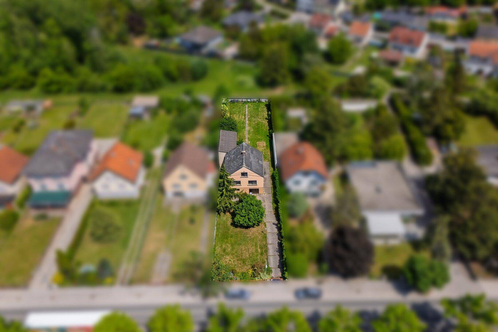 Übersicht aus der Luft eines Hauses mit langem Grundstück, umgeben von viel Grün und Nachbarhäusern.
