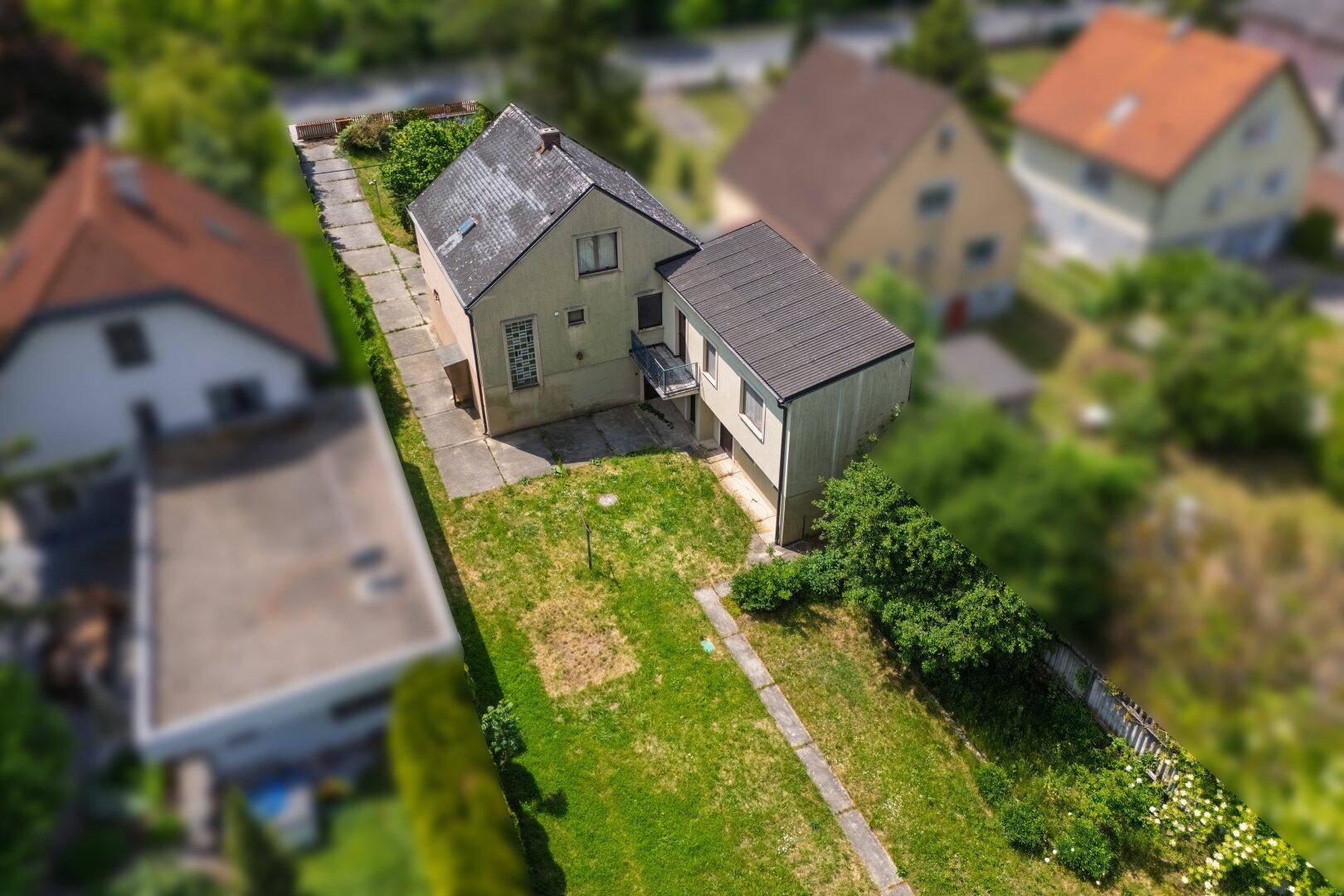 Rückansicht des Hauses mit Garten, kleinem Balkon und angrenzendem Grünbereich.