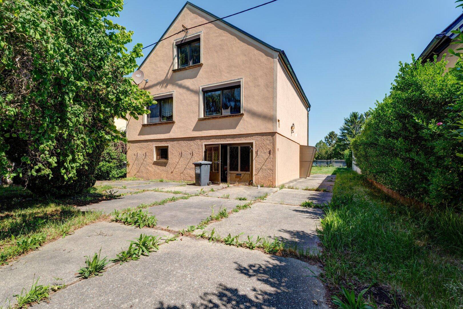 Rückansicht des Hauses mit gepflasterter Zufahrt und viel Grünfläche im Hintergrund.
