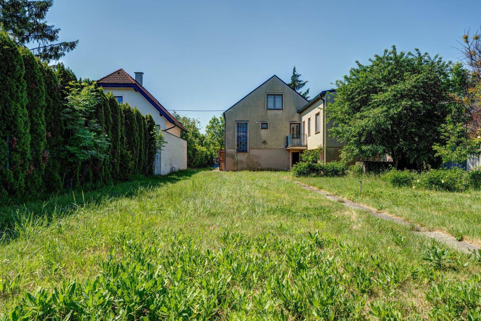 Großer Garten mit Rasenfläche und Blick auf die Rückseite des Hauses und die umliegende Natur.
