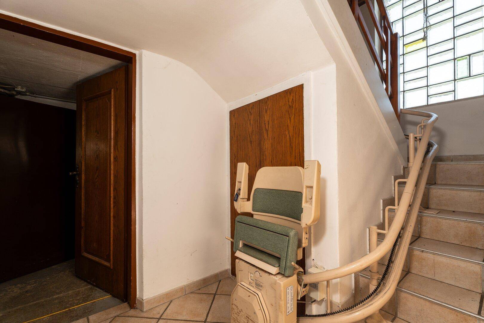 Treppenhaus mit installiertem Treppenlift und Fliesenboden, der Zugang zu den oberen Etagen bietet.