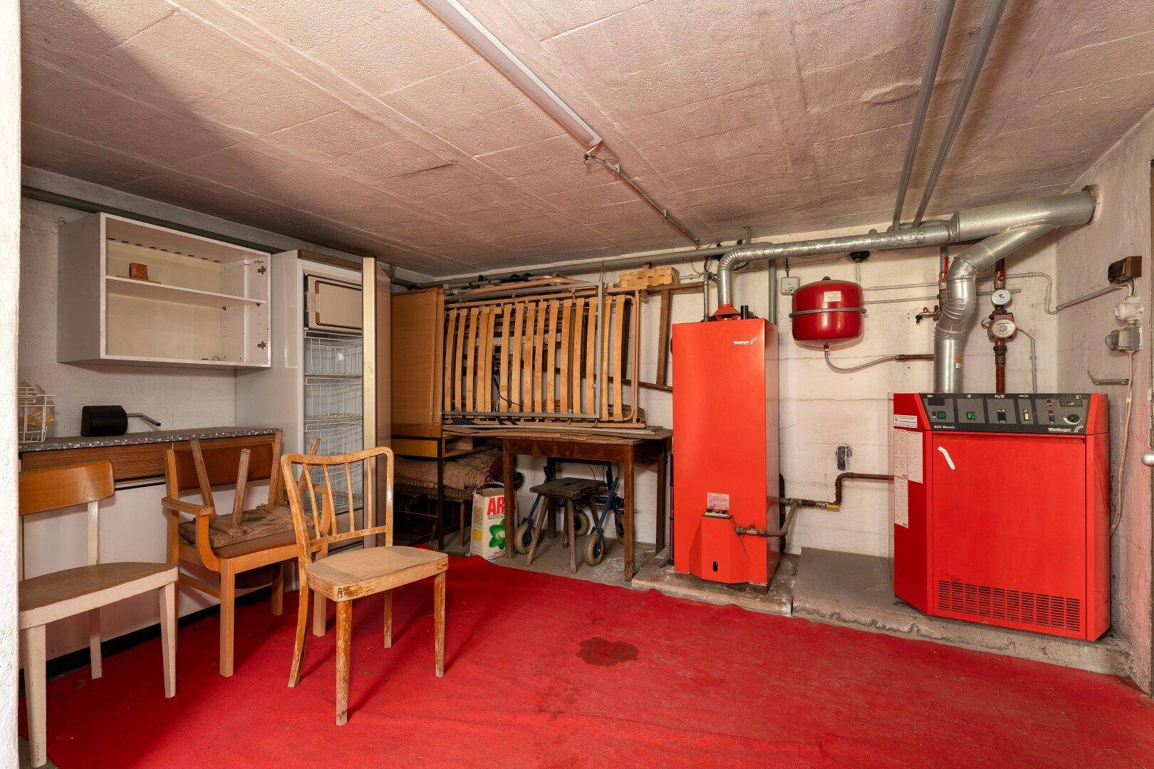 Heizungsraum im Keller mit rotem Heizkessel und verschiedenen Installationen, funktional eingerichtet.