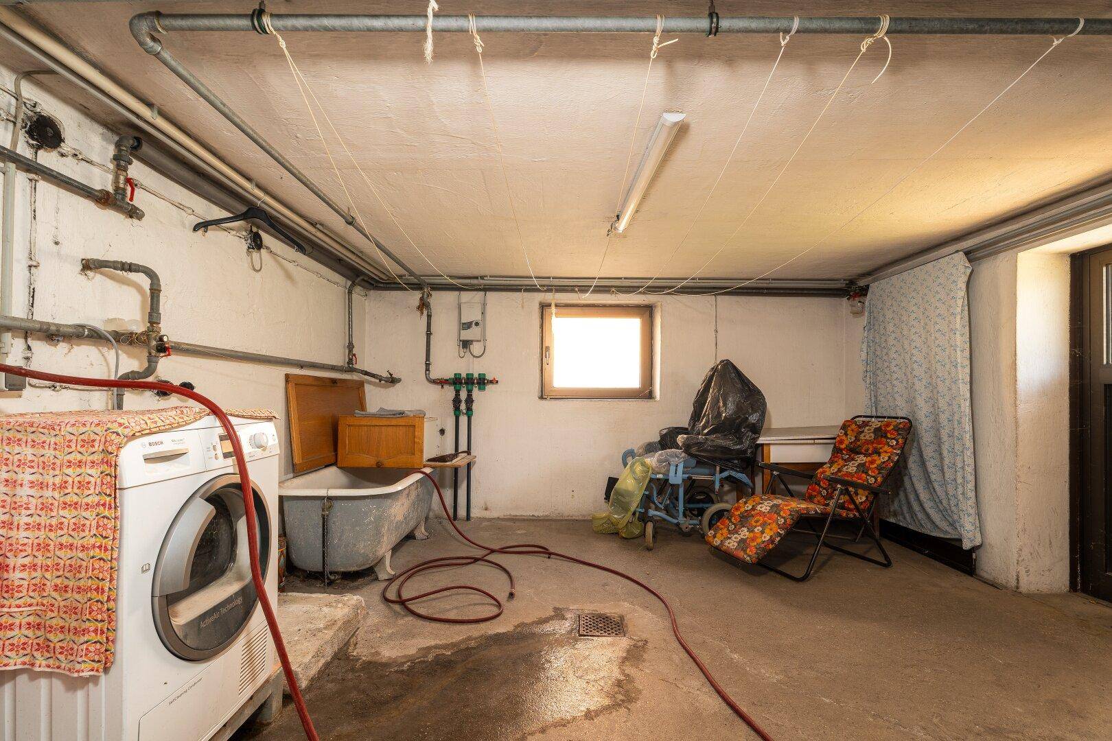 Waschküche im Keller mit Waschmaschine, Trockner und einem kleinen Fenster für Belüftung.