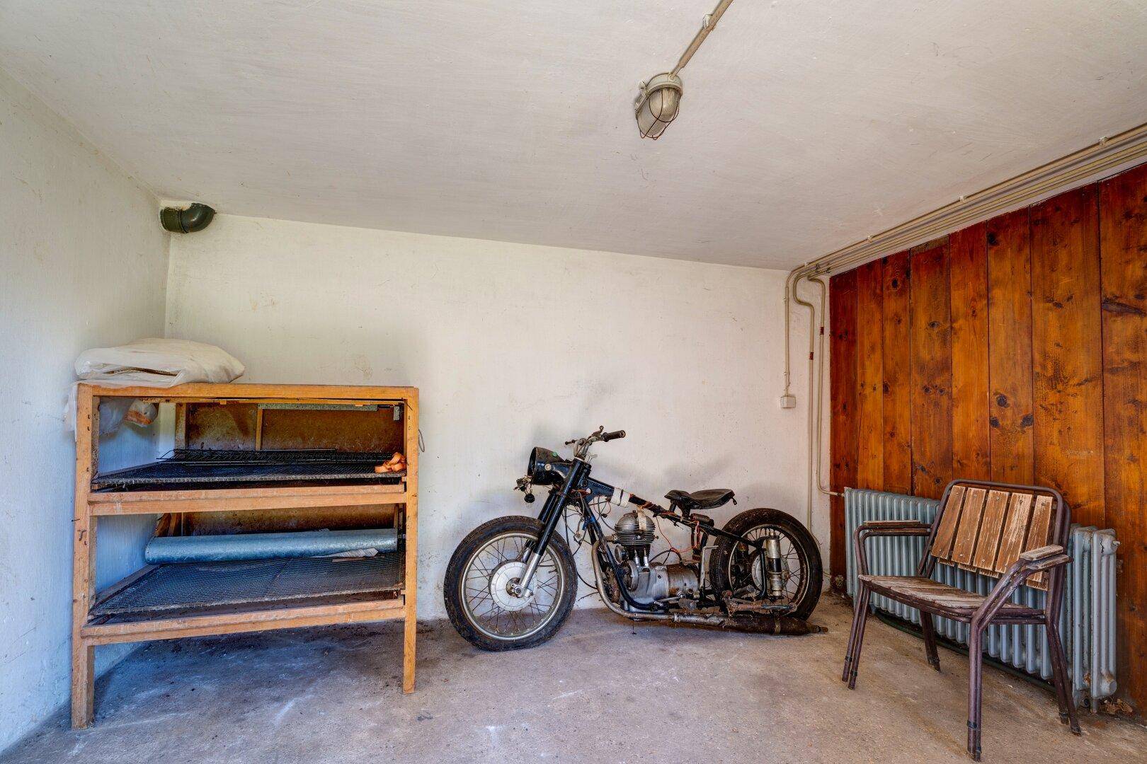 Abstellraum im Keller mit Holzvertäfelung, einem Motorrad und Regalen für diverse Gegenstände.