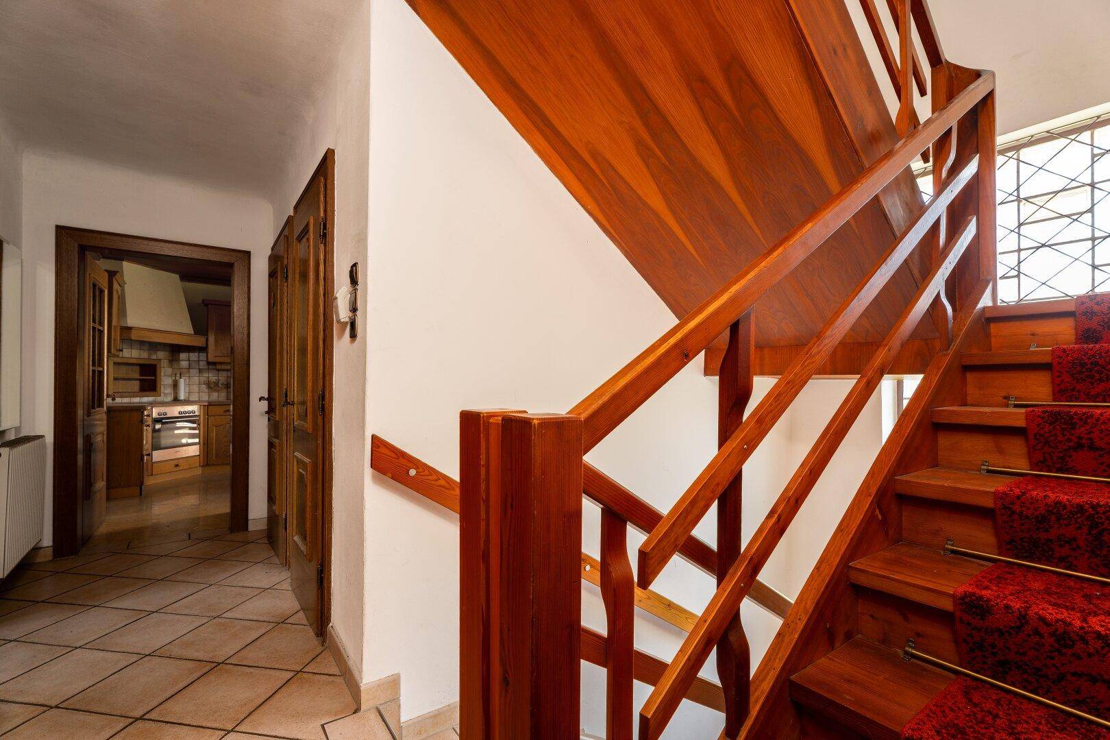 Heller Flur mit Holztreppe und Fliesenboden, der zu den oberen Wohnbereichen führt.
