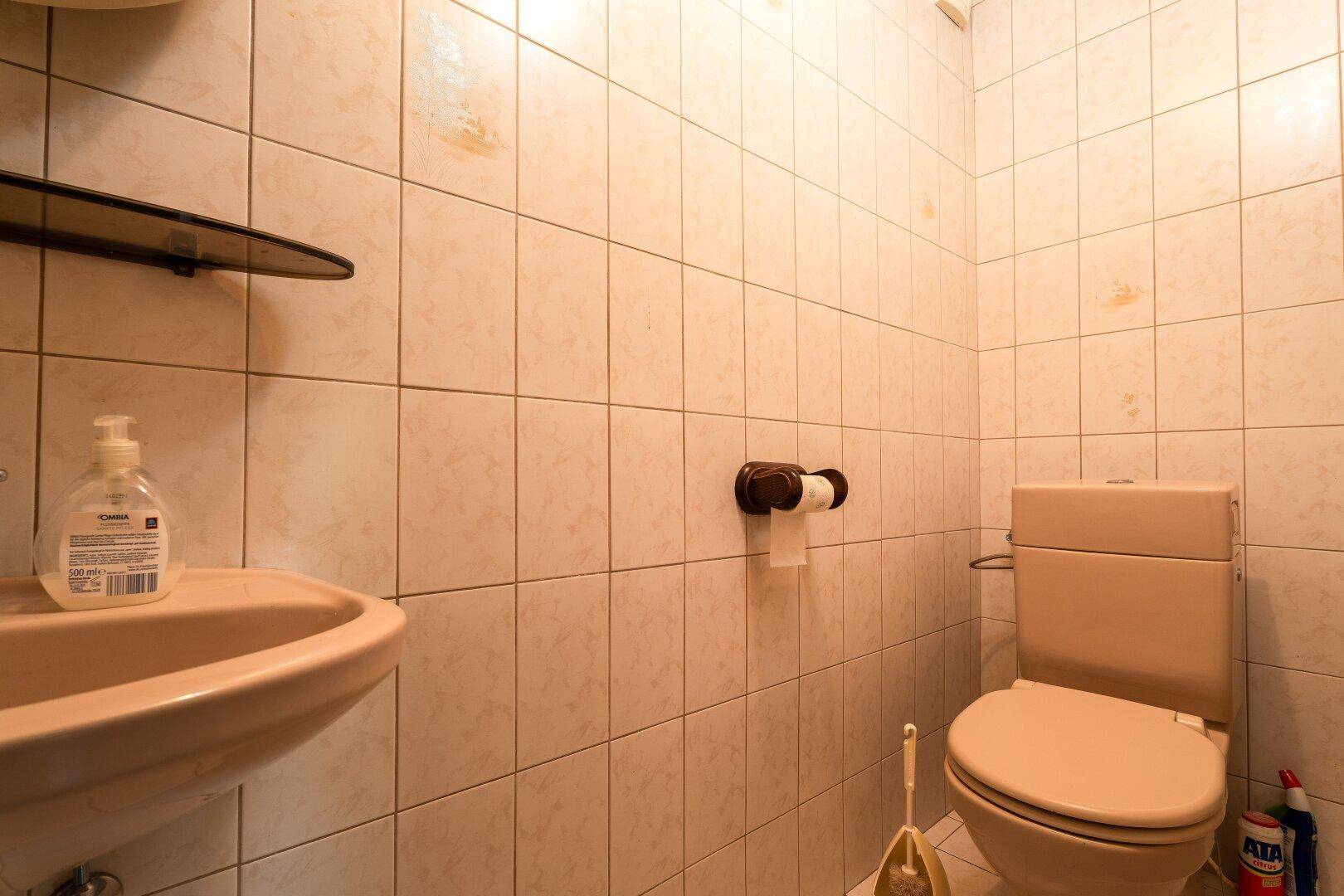 Kleines Gäste-WC mit beigefarbenen Fliesen, Waschbecken und Toilette, einfach ausgestattet.