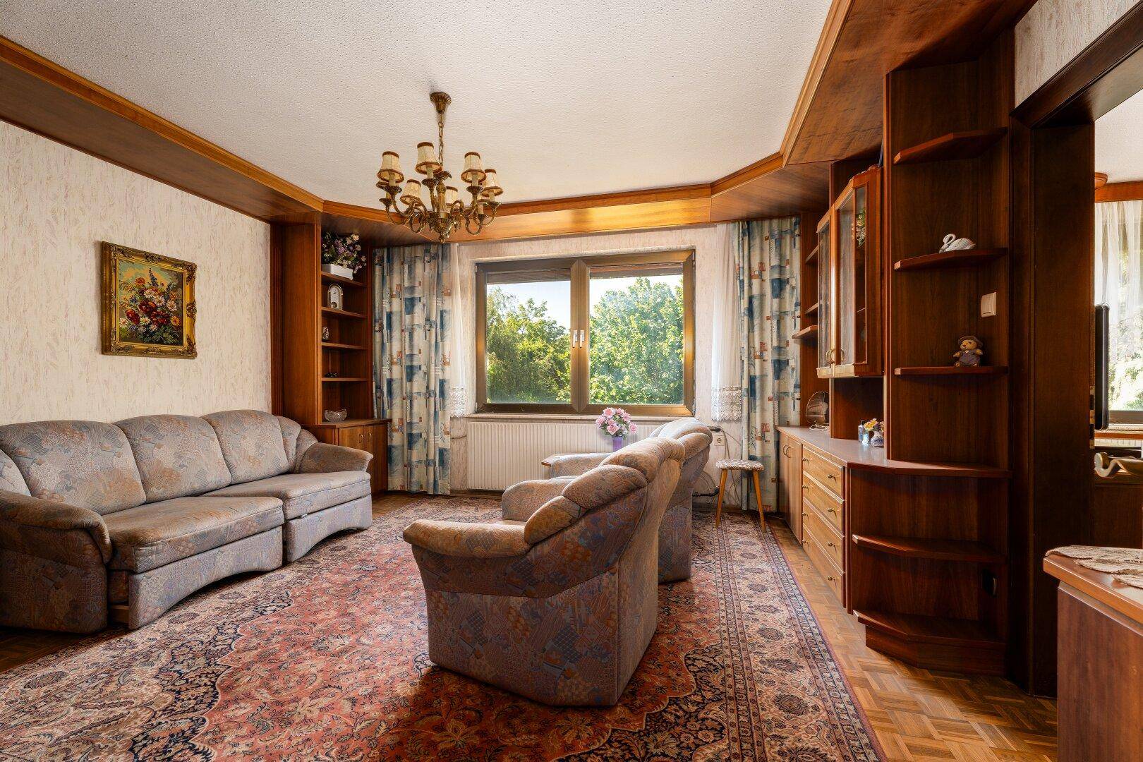 Gemütliches Wohnzimmer mit traditionellen Holzmöbeln, Teppich und Blick ins Grüne.