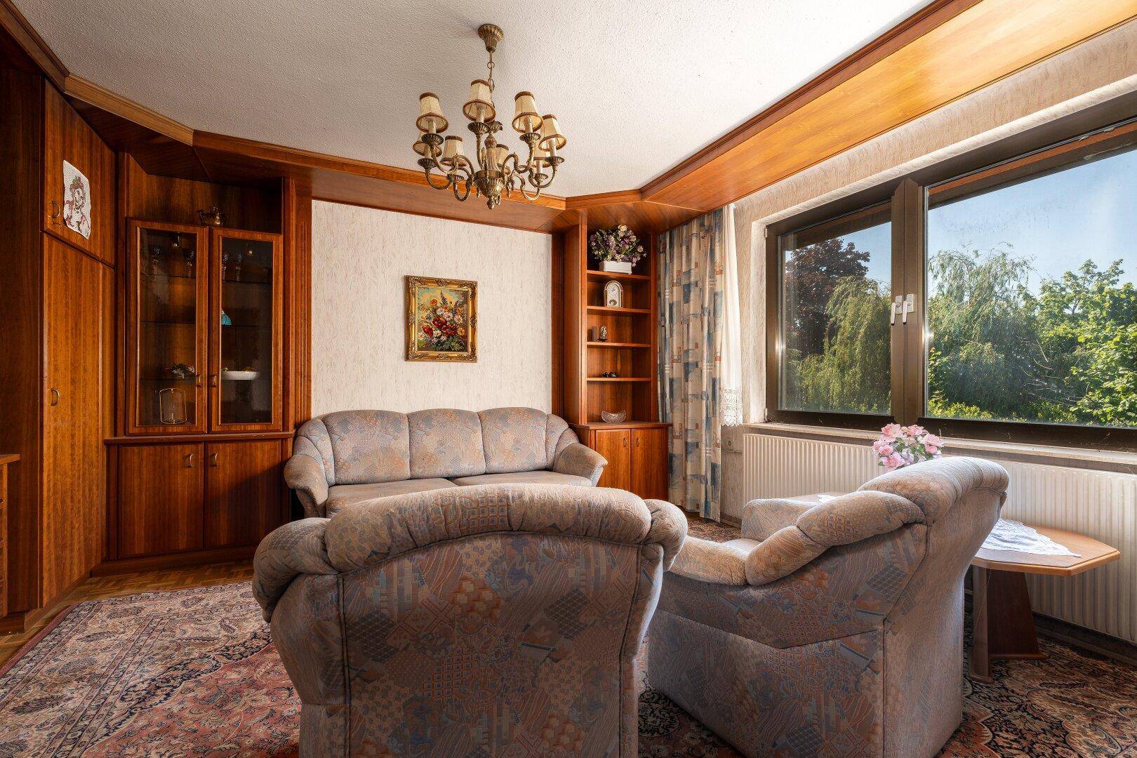 Wohnzimmer mit bequemen Sofas, Holzeinbauten und einem großen Fenster für viel Tageslicht.