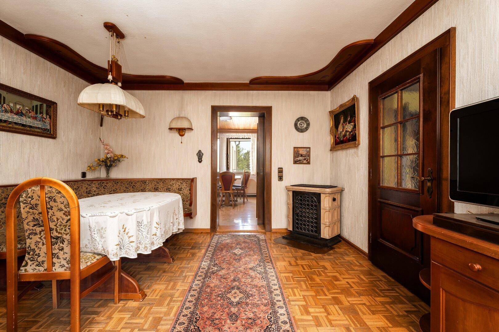 Essbereich mit Holzboden, traditioneller Sitzbank und einem Kachelofen für gemütliche Wärme.