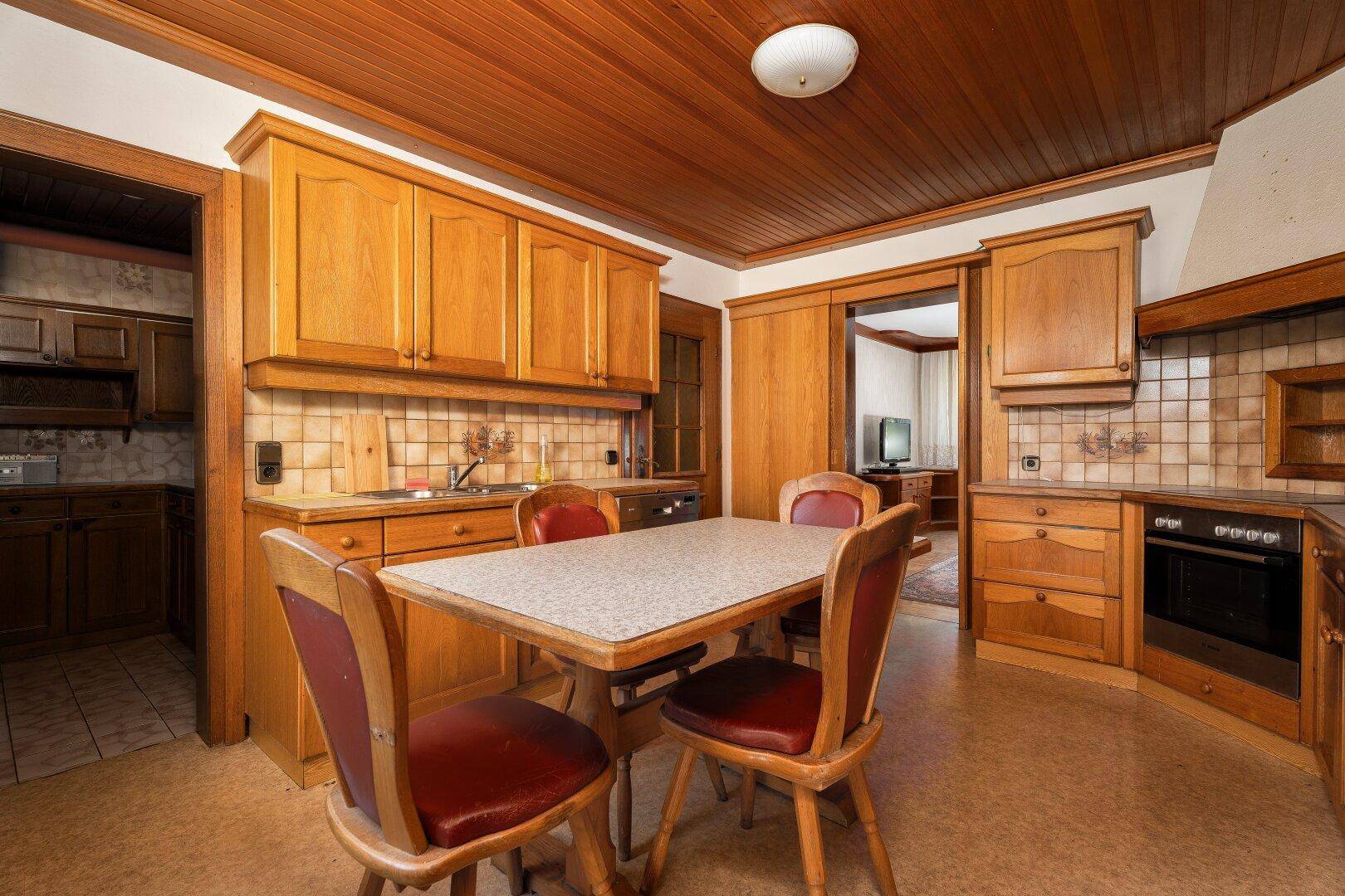 Traditionelle Küche mit Holzschränken, Esstisch und Fliesenrückwand, funktional eingerichtet.