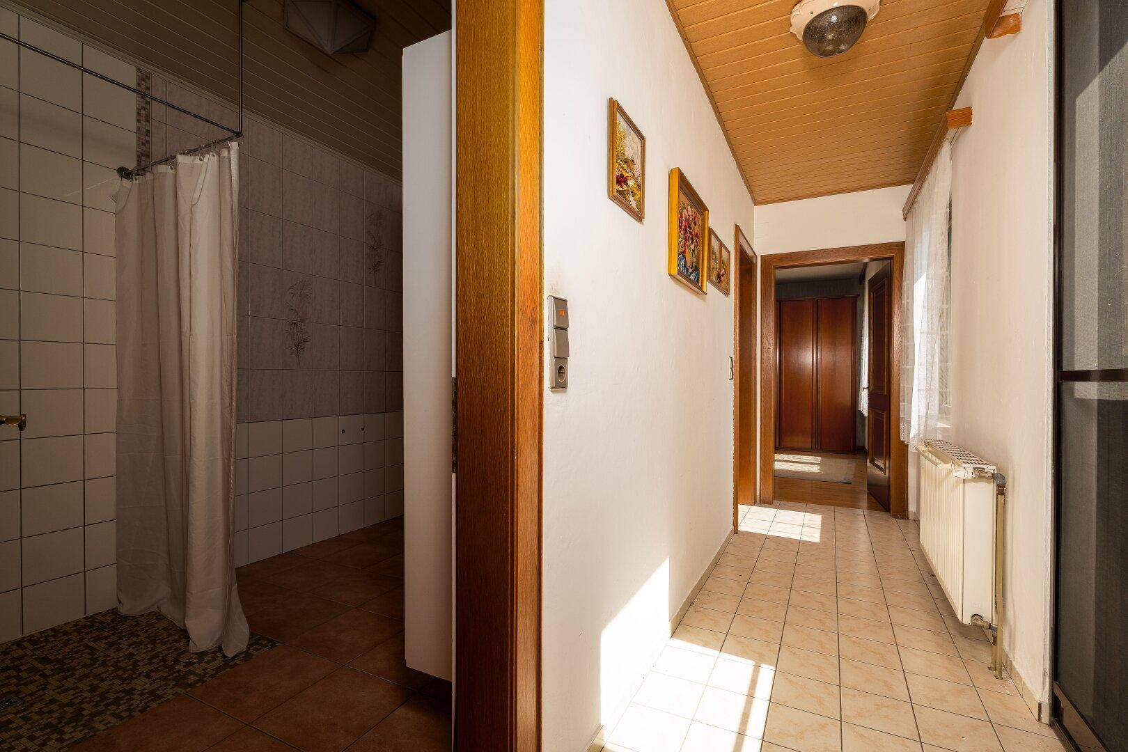 Heller Flur mit Fliesenboden, der zu einem Badezimmer mit Duschbereich führt.