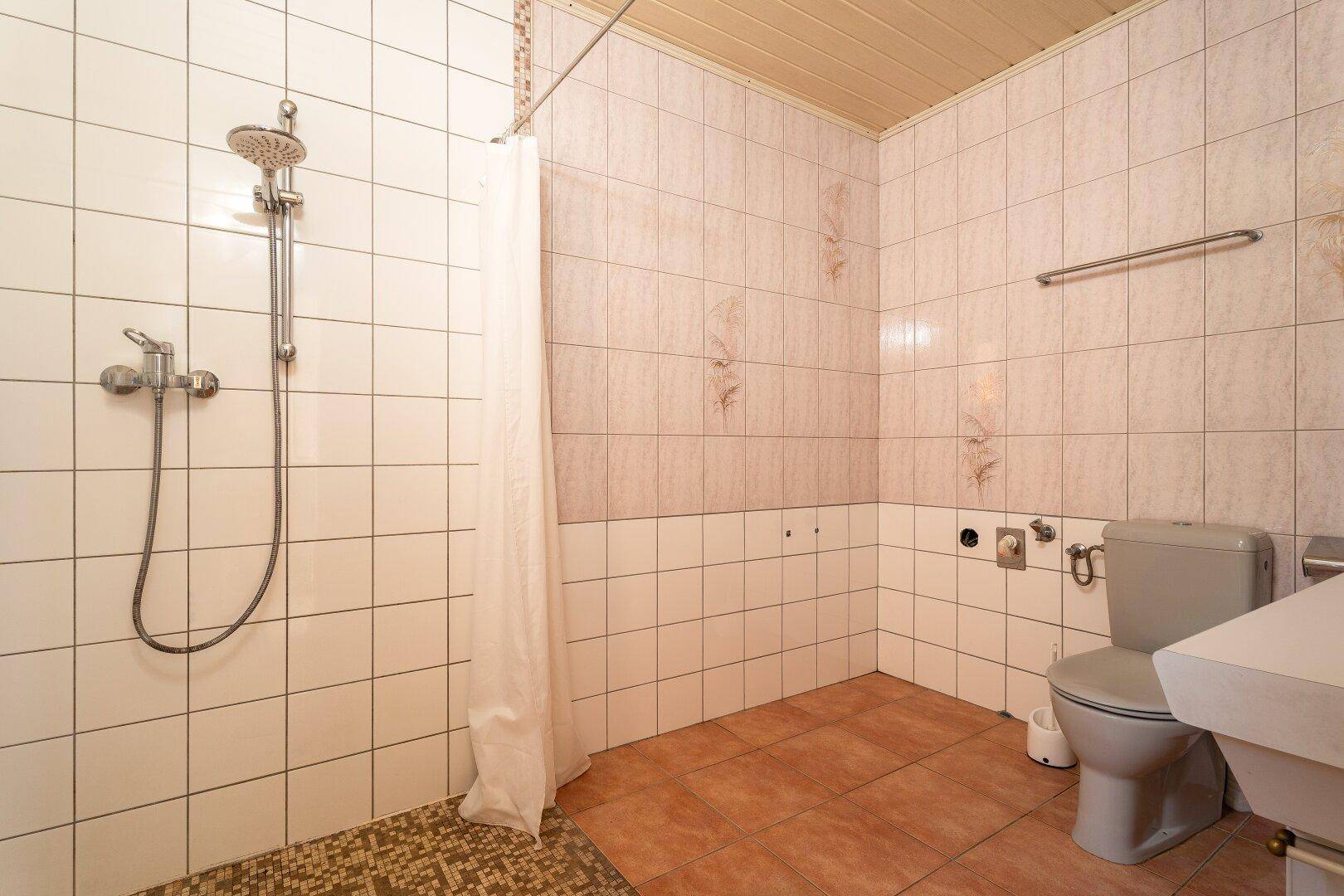 Badezimmer mit Duschbereich, Toilette und hellen Fliesen, einfach und funktional.