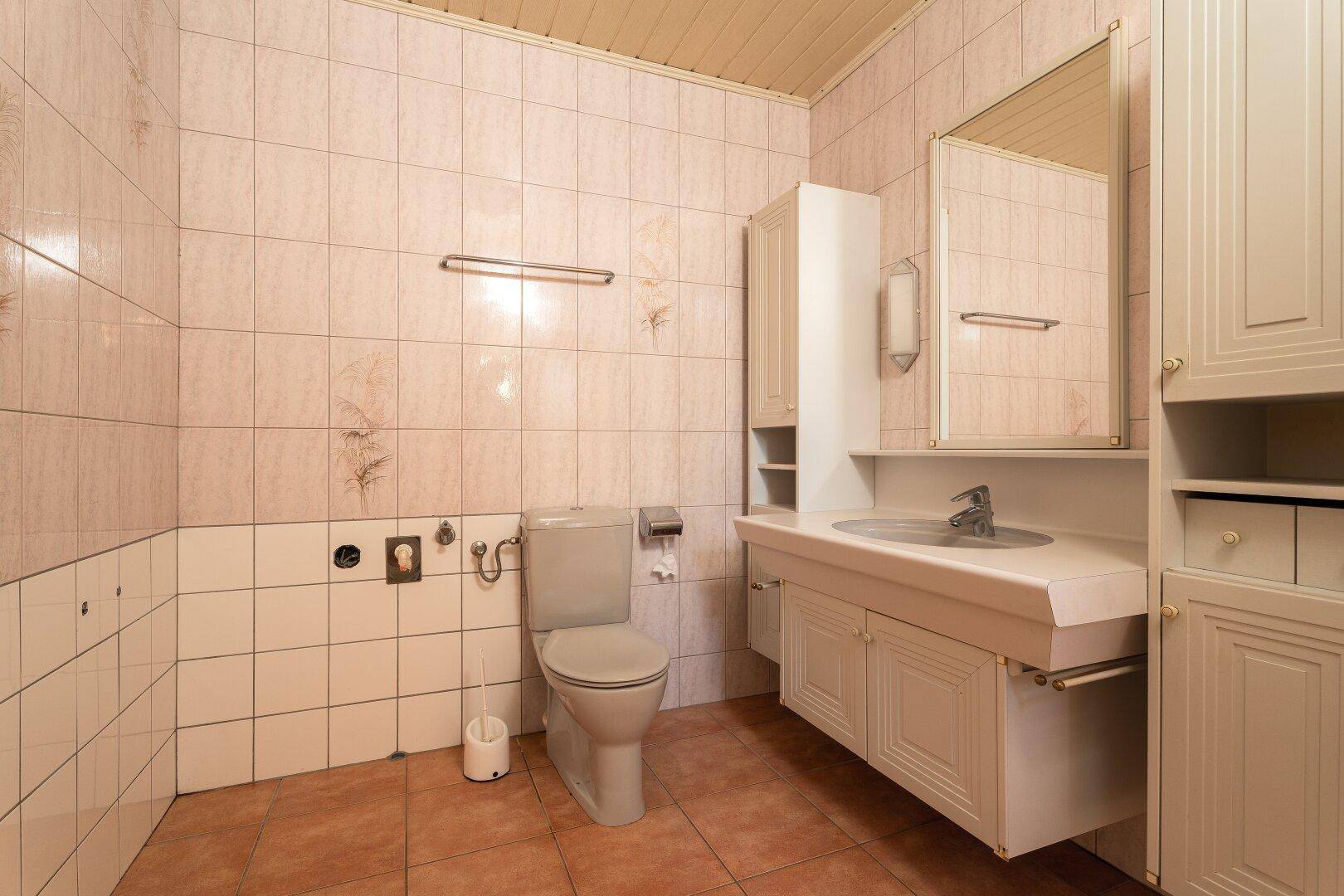 Badezimmer mit Waschtisch, Spiegelschrank und hellen Fliesen, bietet Stauraum und Funktionalität.