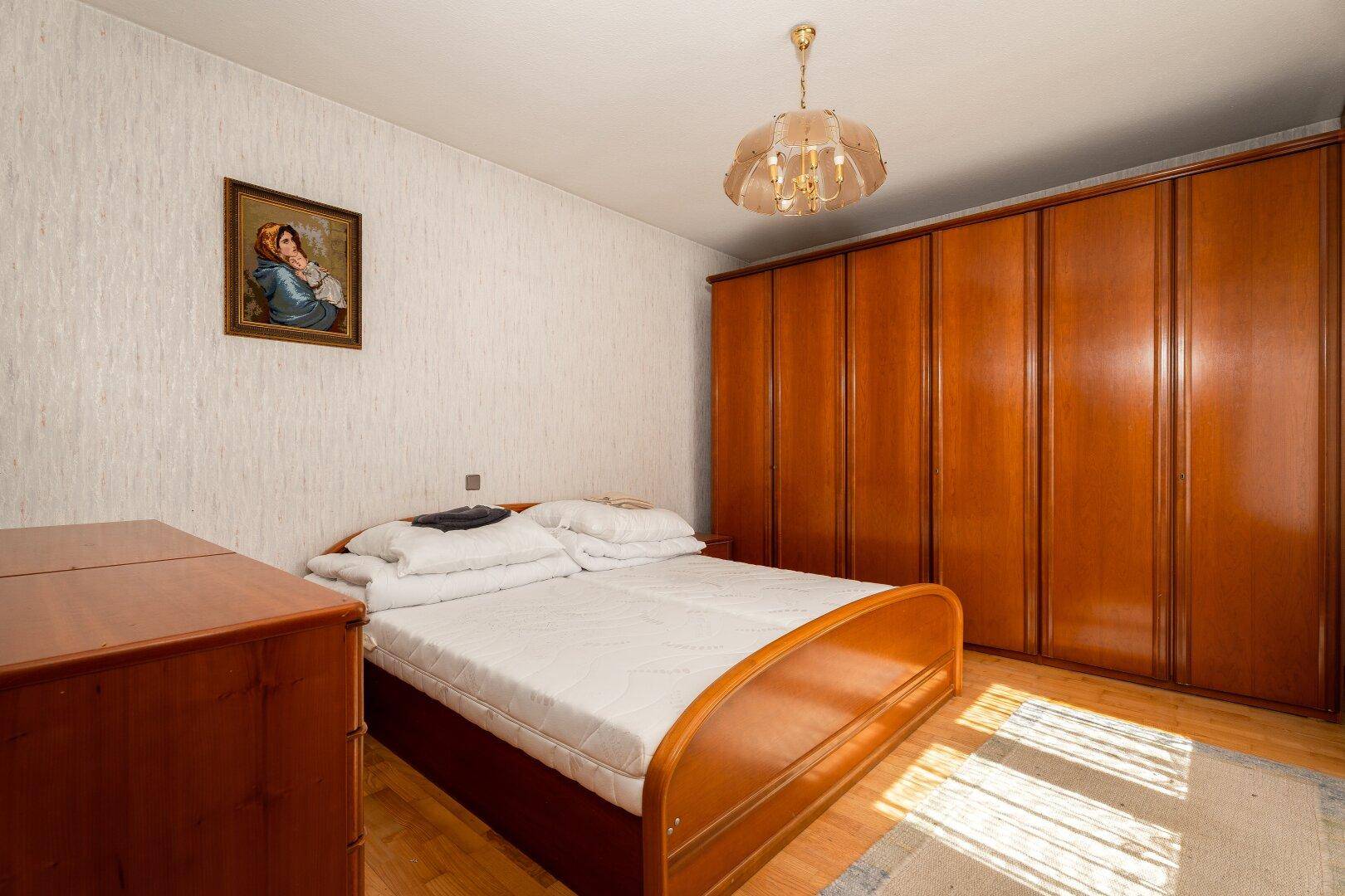 Schlafzimmer mit Doppelbett, großem Holzschrank und Parkettboden, hell und geräumig.