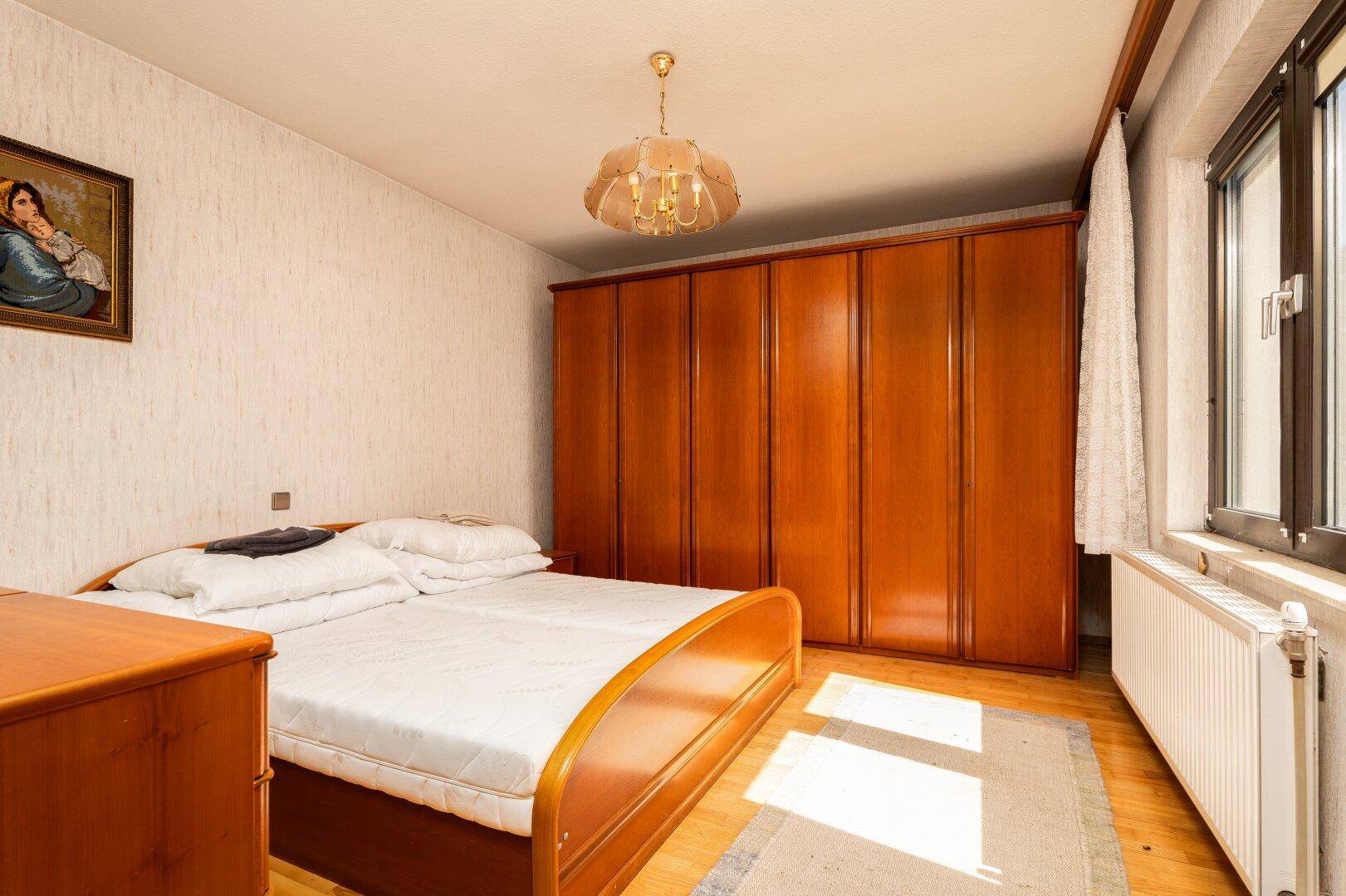 Helles Schlafzimmer mit Holzboden, großem Kleiderschrank und Fenster für viel Tageslicht.