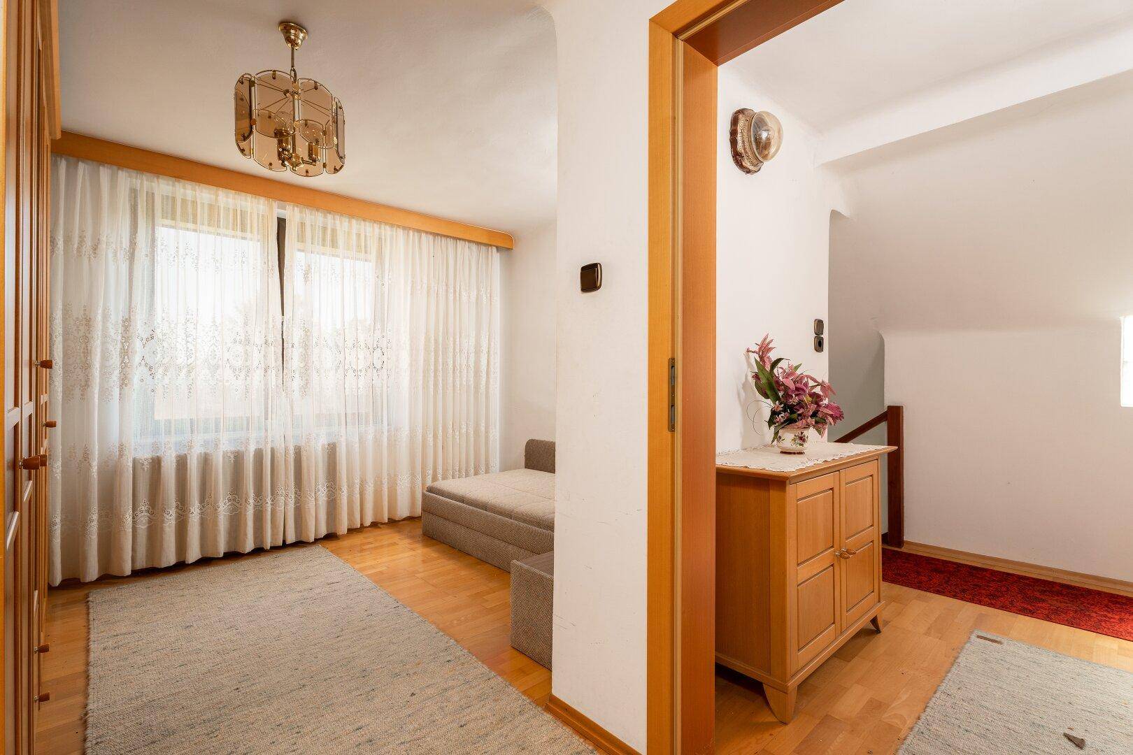 Heller Flur mit Sofa, Holzschrank und Zugang zu weiteren Räumen sowie einer Treppe.
