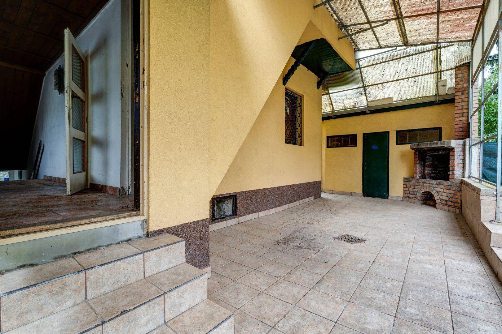 Geräumige überdachte Terrasse mit Fliesenboden und gemauertem Grillbereich.