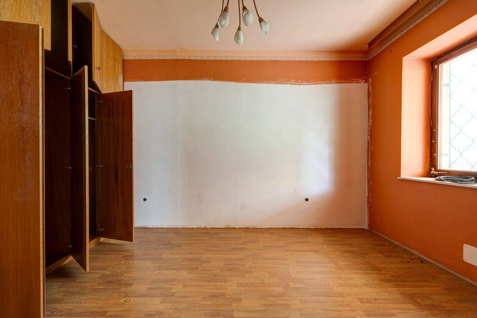 Leeres Zimmer mit Holzfußboden, orangefarbenen Wänden und Einbauschränken.