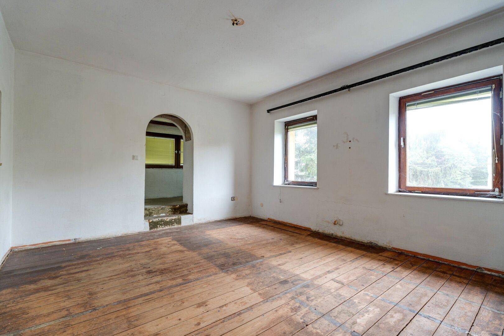 Leeres Zimmer mit Holzdielenboden, weiß gestrichenen Wänden und einem Rundbogen.
