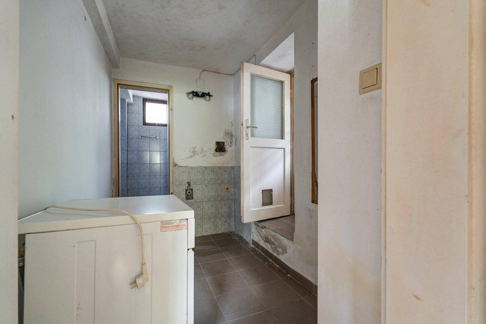 Hauswirtschaftsraum mit Waschmaschine und Zugang zu einem weiteren Raum.