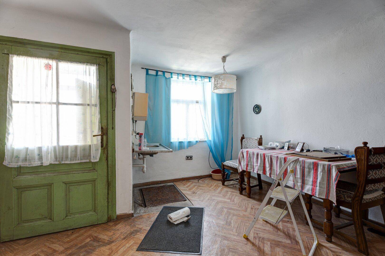 Gemütliche Wohnküche mit Esstisch, Holzparkett und einem Fenster mit blauen Vorhängen.