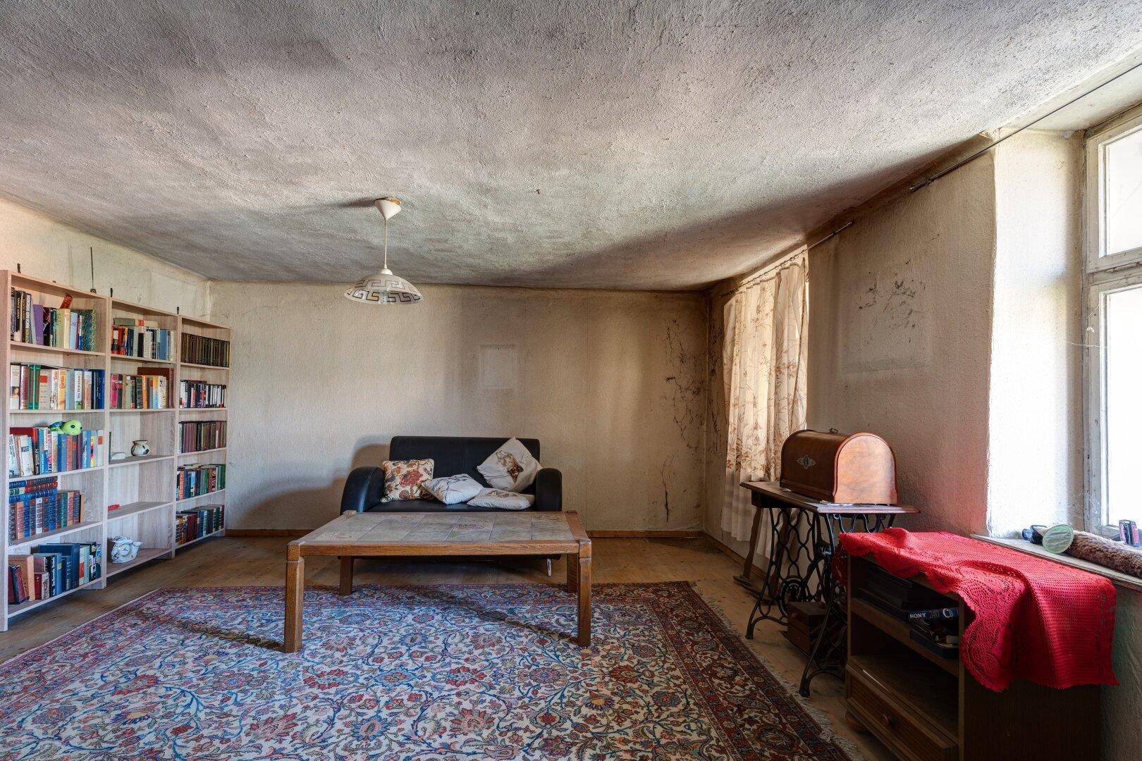 Wohnzimmer mit Sofa, Couchtisch, Bücherregal und einem gemusterten Teppich auf Holzfußboden.