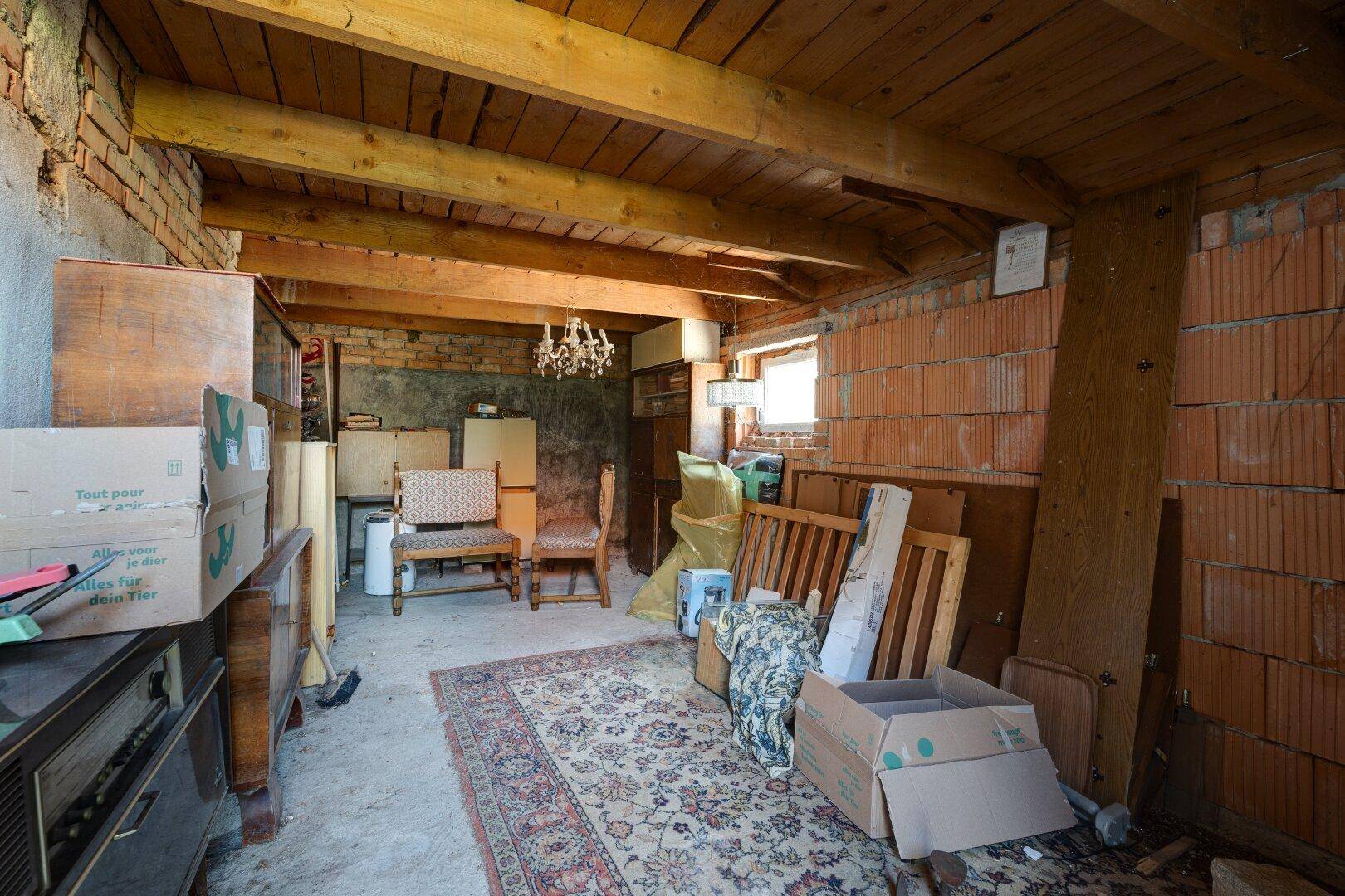 Lagerraum mit sichtbaren Holzbalken, unverputzten Ziegelwänden und verschiedenen Gegenständen.