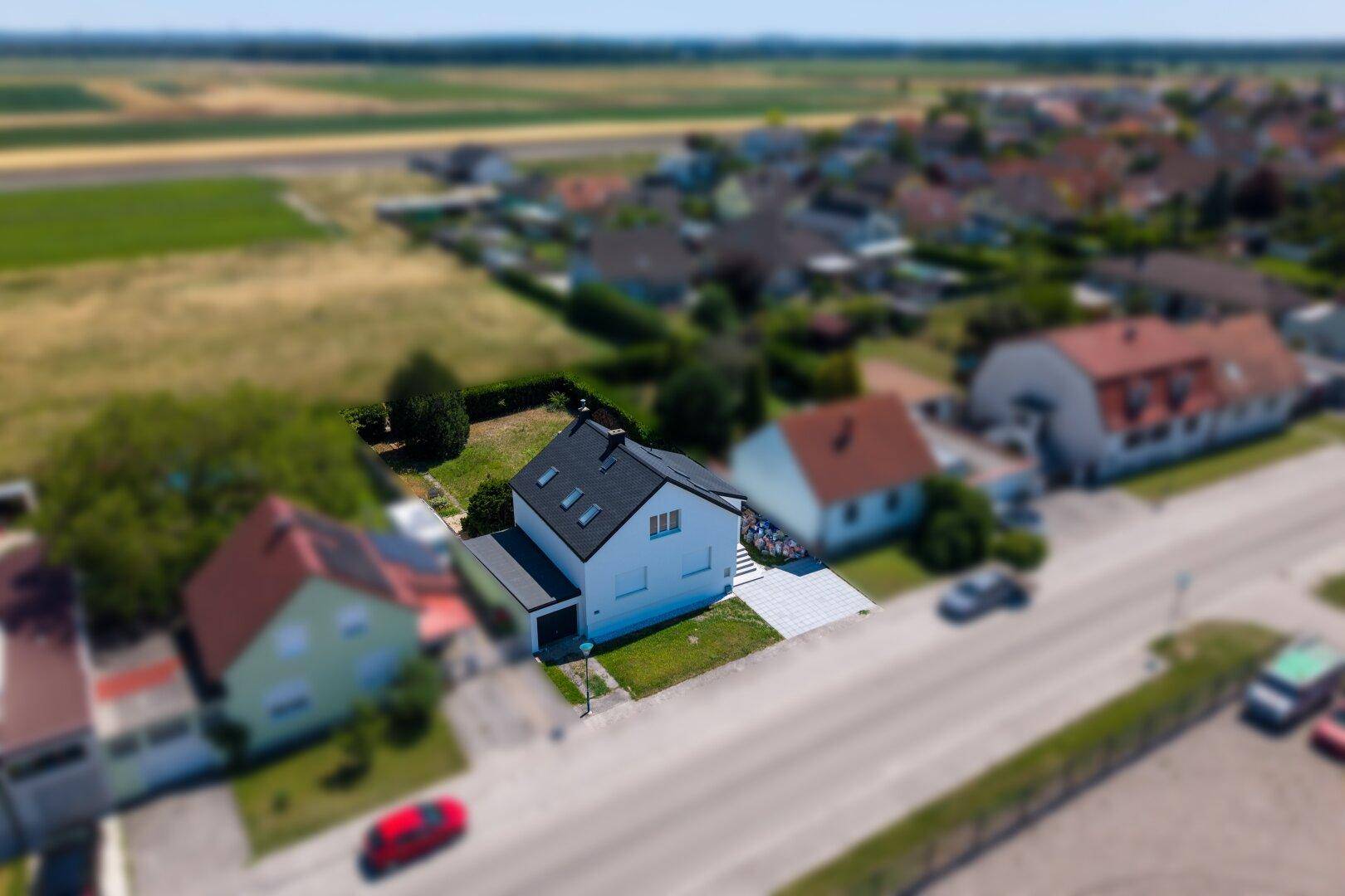 Luftaufnahme des Einfamilienhauses und der umliegenden Siedlung mit Feldern im Hintergrund.
