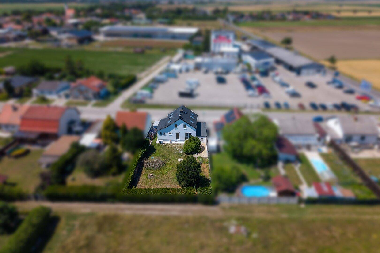 Luftaufnahme eines Einfamilienhauses mit Garten und ländlicher Umgebung unter blauem Himmel.