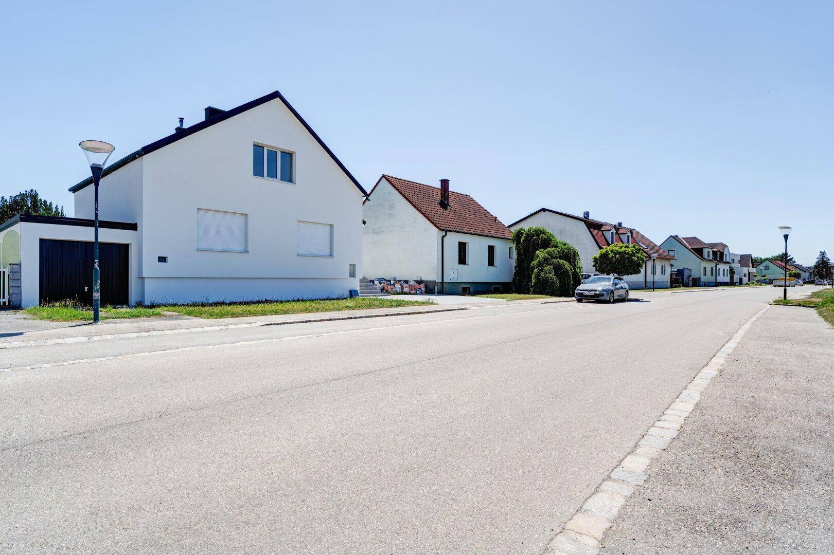 Blick auf die ruhige Wohnstraße mit dem modernen Einfamilienhaus und Nachbargebäuden.