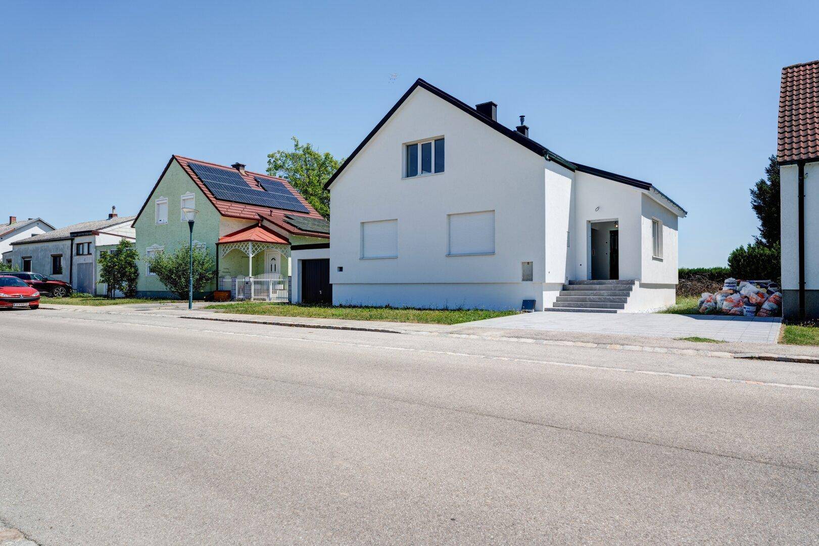 Weitläufige Straßenansicht mit dem weißen Einfamilienhaus und der ländlichen Umgebung.