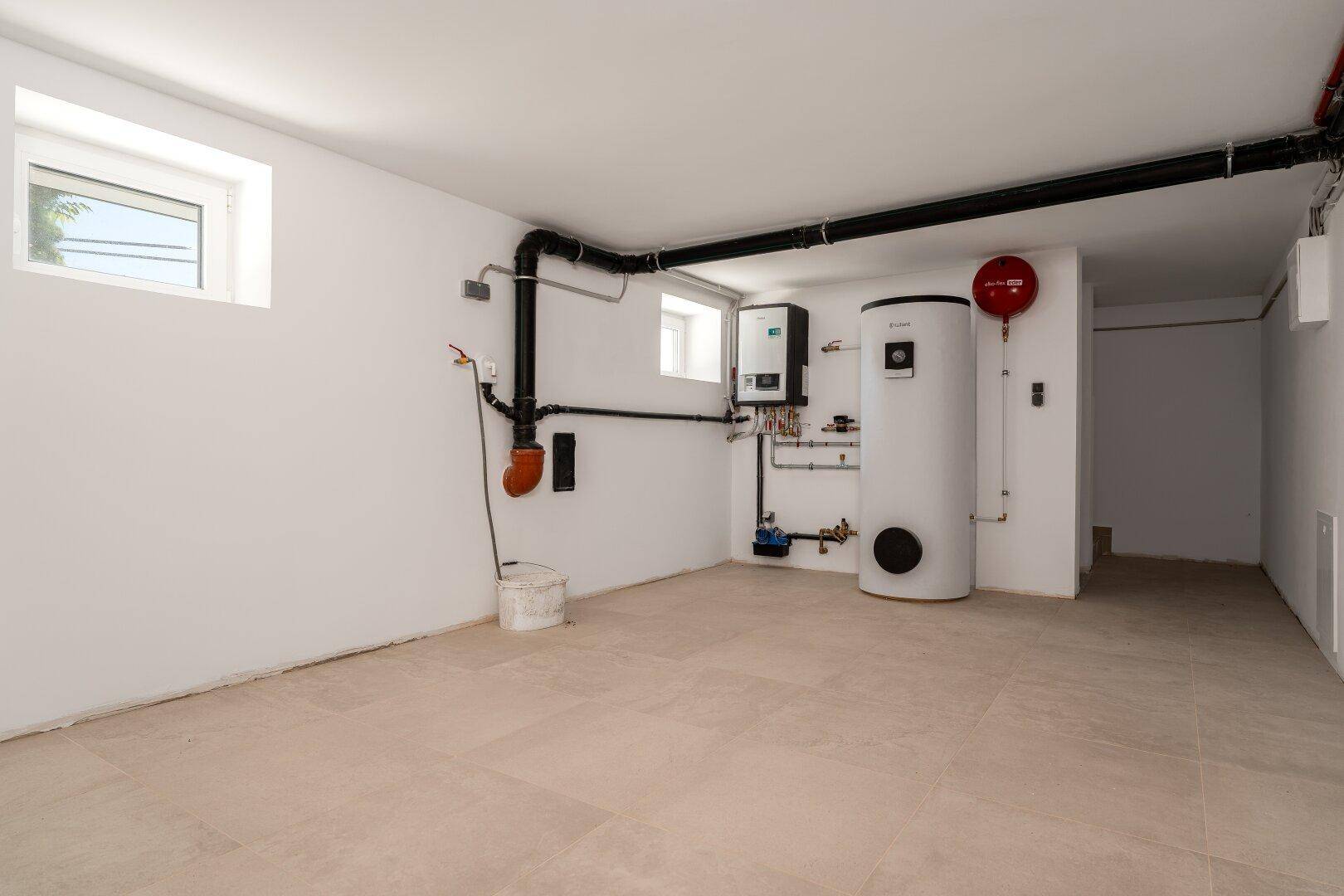 Heller Hauswirtschaftsraum im Keller mit Heizungsanlage, Leitungen und Fliesenboden.