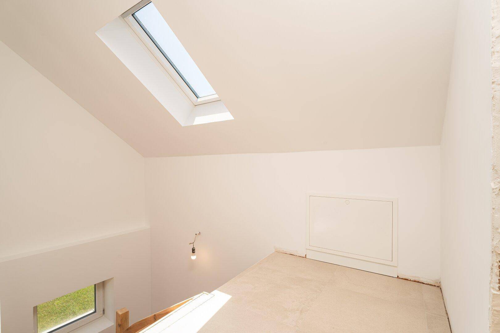 Heller Dachbodenraum mit schrägen Wänden und einem großen Dachfenster für Tageslicht.