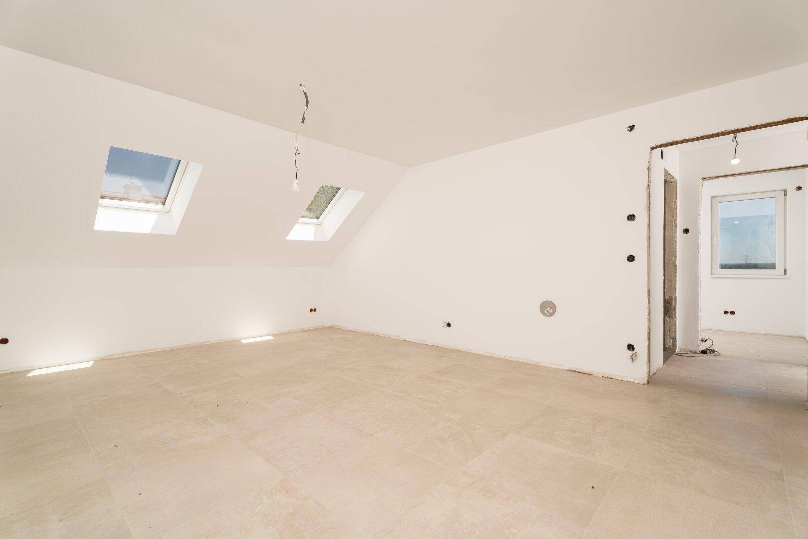 Geräumiger Dachbodenraum mit Fliesenboden, zwei Dachfenstern und vorbereiteten Anschlüssen.