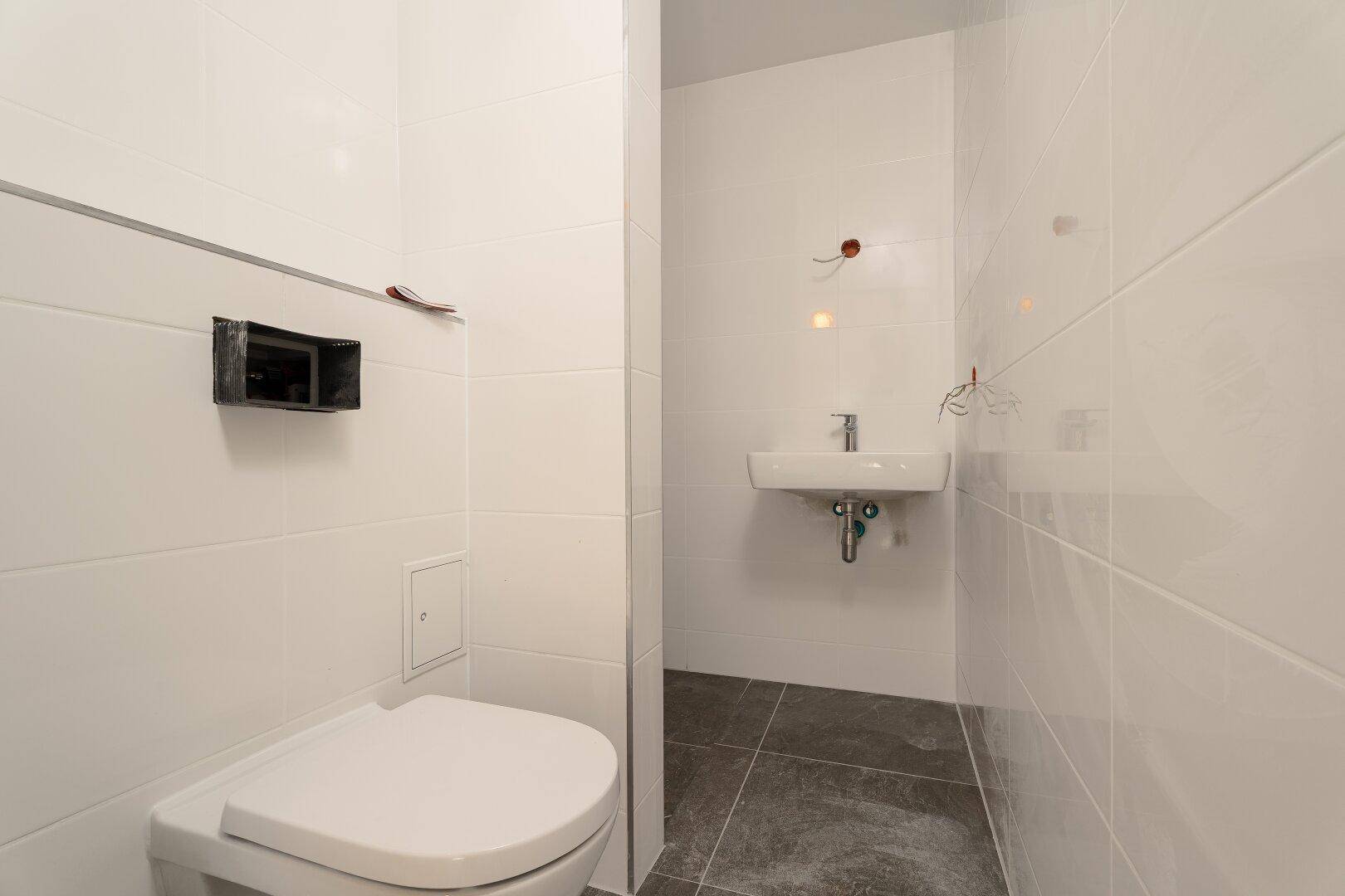 Modernes Gäste-WC mit weißen Wandfliesen, Hänge-WC und kleinem Waschbecken.